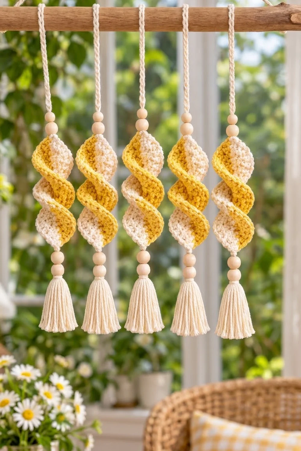 Five crocheted spiral ornaments in yellow and cream with wooden beads and tassels hanging from a wooden rod.