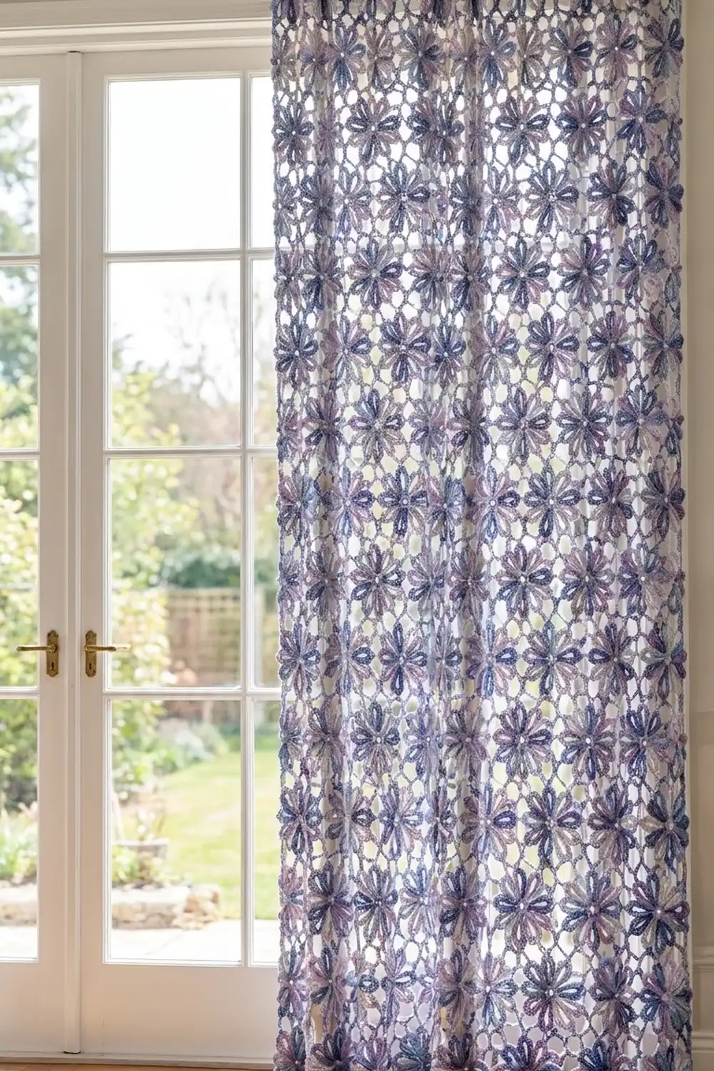 A purple floral lace curtain panel hangs beside white French doors overlooking a garden.