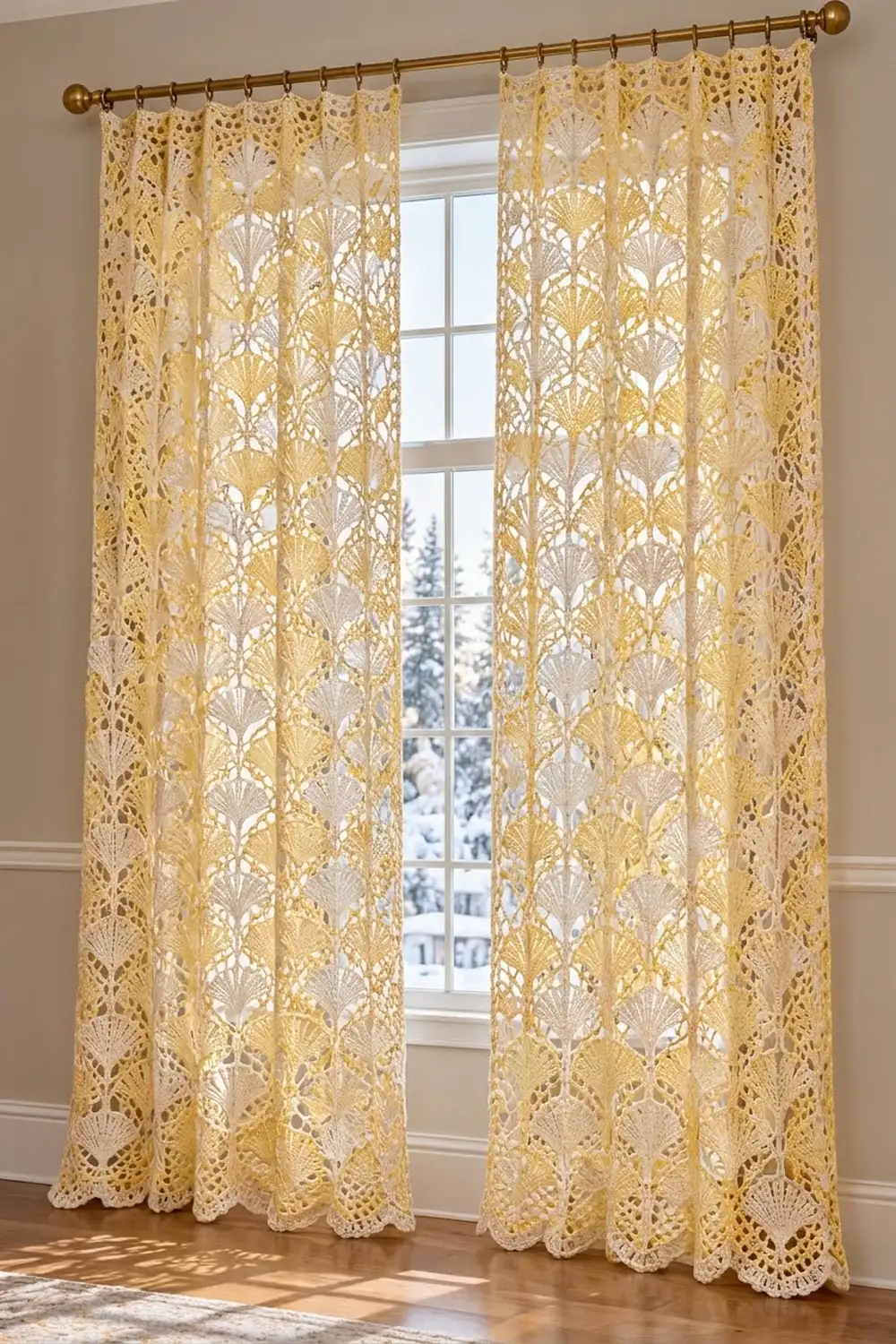 Pair of yellow lace curtains with shell pattern hanging from brass rod on window overlooking snowy landscape.