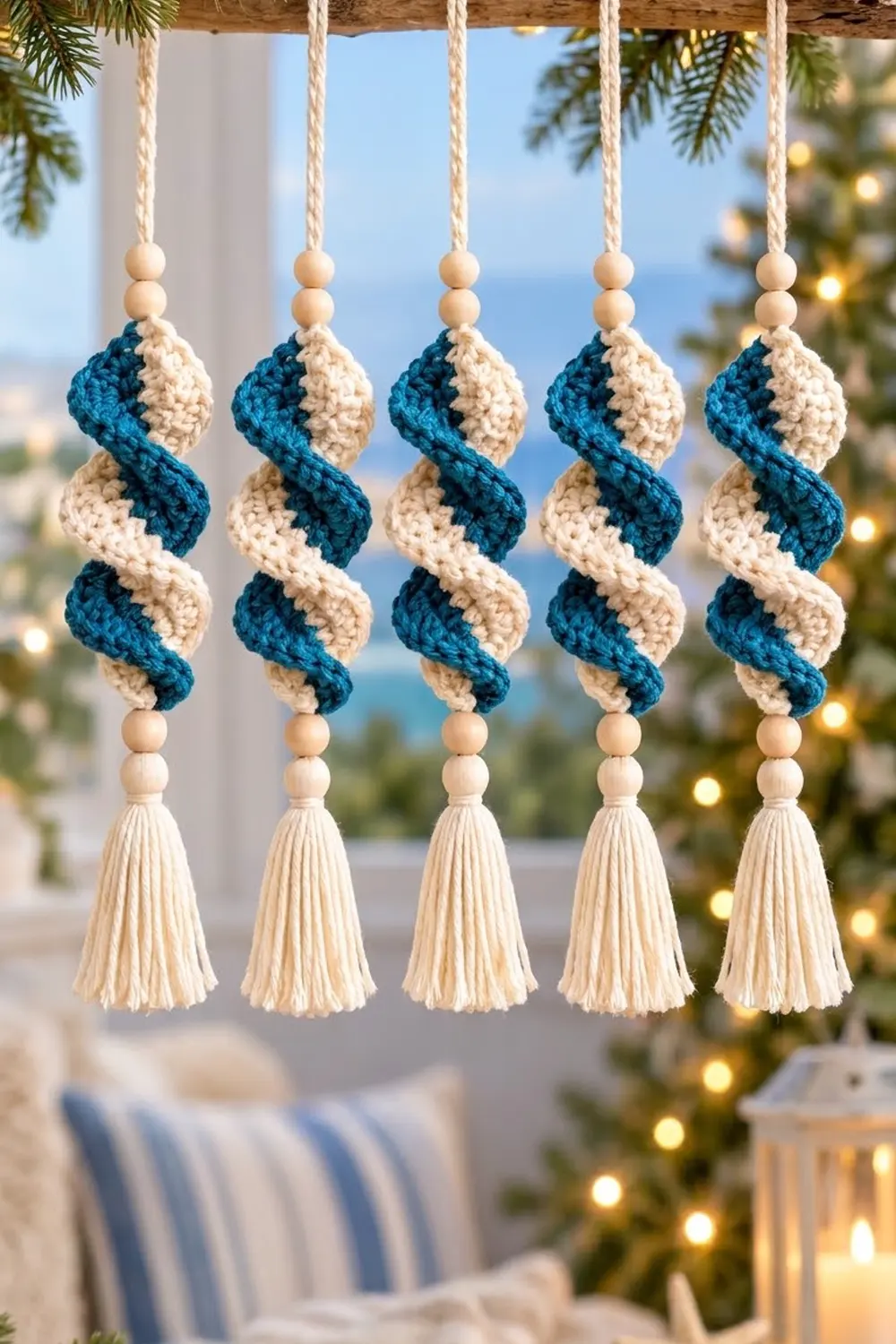Five handmade crocheted ornaments in cream and navy with wooden beads hang near a decorated Christmas tree.