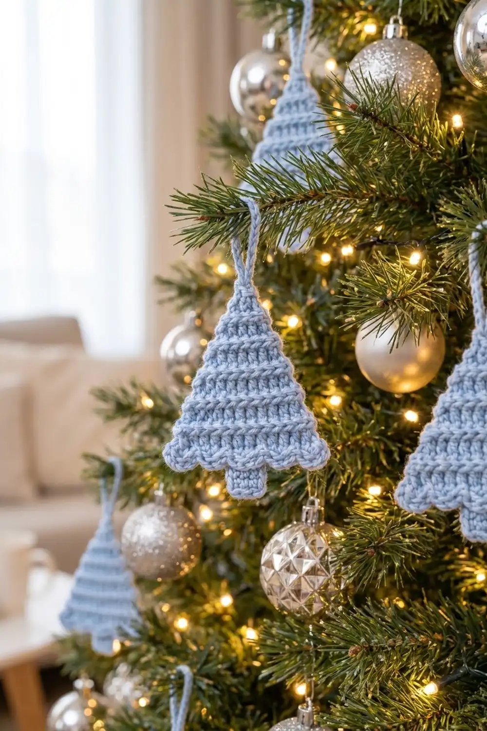 Blue crocheted Christmas tree ornaments hang among green branches, warm white lights, and metallic baubles.