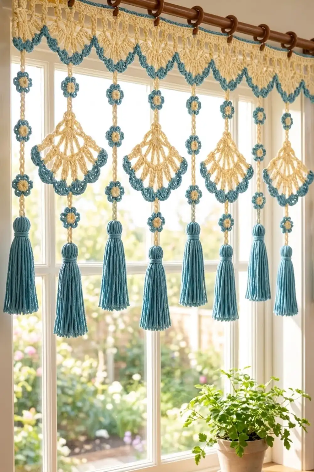 Crocheted cream and teal window valance with shell motifs and hanging tassels, displayed in a sunny window overlooking a garden.