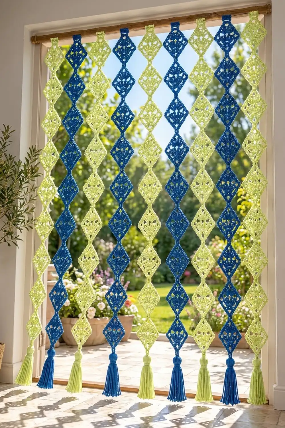 Crocheted curtain with alternating navy and lime diamond shapes and tassels hanging in a sunny doorway overlooking a garden.