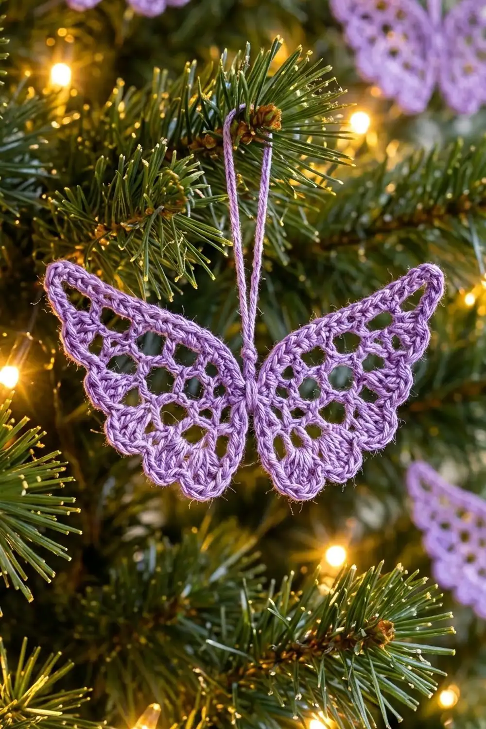 Delicate purple crocheted butterfly ornament hangs on an evergreen bough surrounded by warm golden lights and soft purple blooms.
