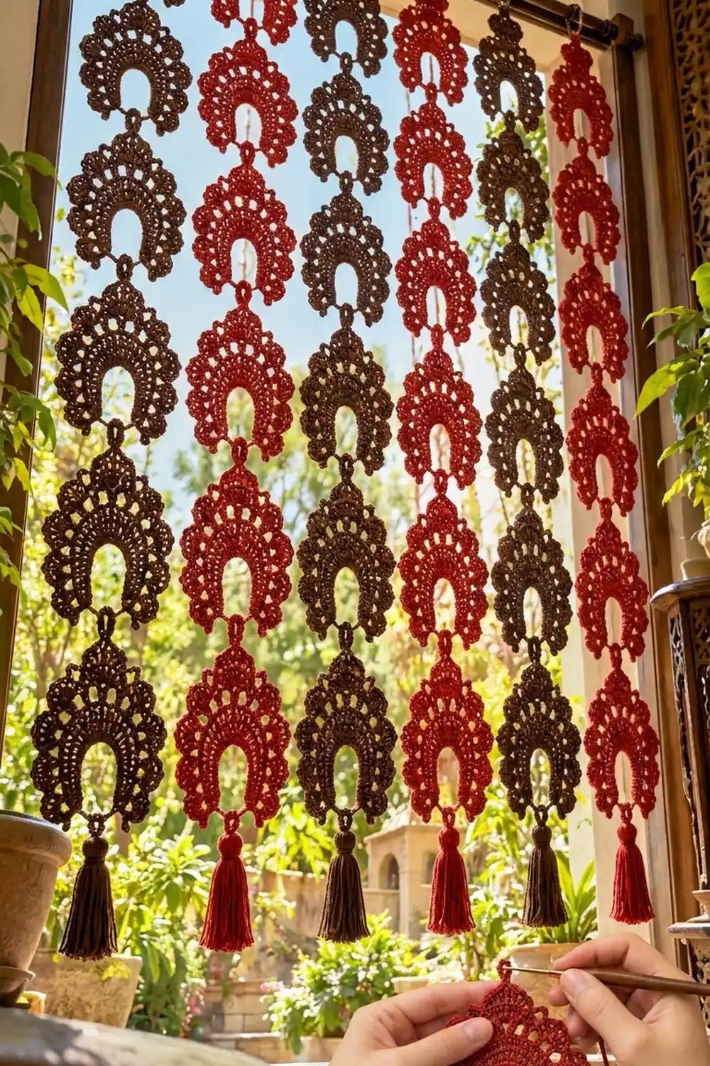 Burgundy and brown crocheted doilies with tassel trim hang in a window, backlit by green garden foliage.